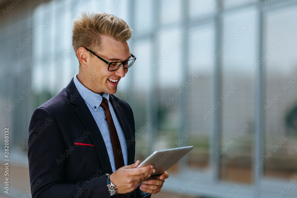 Elegant young businessman using his PC tablet. Portrait of a Male executive manager in trendy clothes with tablet pc in front of office building. Modern technology concept Elegant young businessman using his PC tablet. Portrait of a Male executive manager in trendy clothes with tablet pc in front of office building. Modern technology concept
