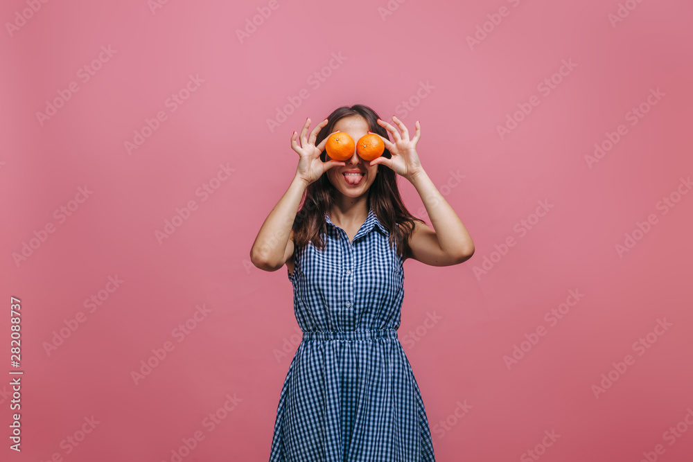Girl closed her eyes with oranges and shows tongue on pink background Girl closed her eyes with oranges and shows tongue on pink background