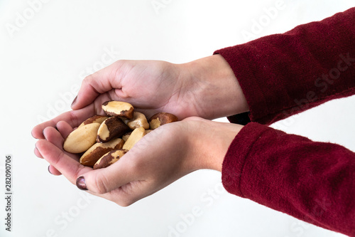 Close up of girl hand with painted nails holding Brazil nuts (Bertholletia excelsa) on white background. Brazil nuts are protein, carbohydrate, and fat, very nutritious and healthy food.