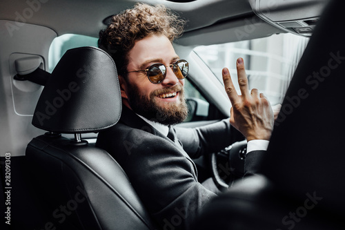 Handsome young businessman in full suit greetings with friends while driving a new car. View from behind. photo