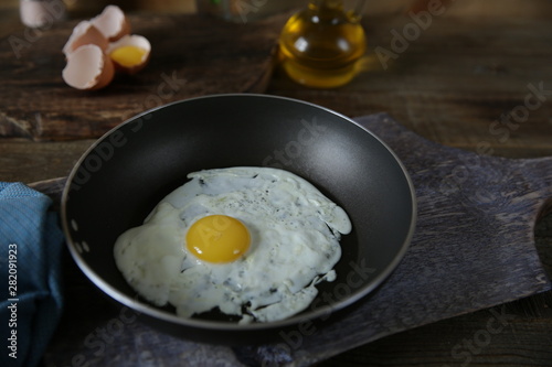 Close-up. Frying pan with frying egg with yolk on a wooden cutting board with ingredients for the preparation of fried eggs: raw eggs, olive oil, salt, parsley. 