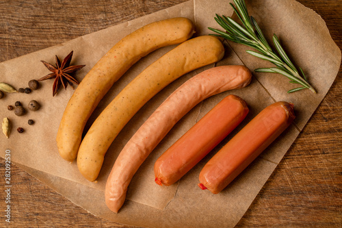Assorted raw sausages and spices on paper, on wooden background  