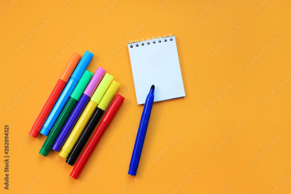 Felt-tip pens and blank notepad on yellow background. Concept of the educational process, study at school. Back to school concept. Felt-tip pens and blank notepad on yellow background. Concept of the educational process, study at school. Back to school concept.