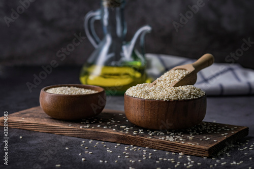 White sesame in a wooden spoon on dark table, Sesame oil in jar and seeds concept.