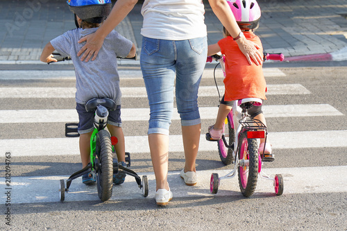 Mother goes pedestrian crossing with children on bicycles. A woman with children crossing the road in the city. Back view. photo