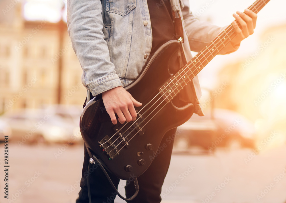 Street young musician, dressed in a denim jacket, and illuminated by bright sunlight, playing electric bass guitar powerful track