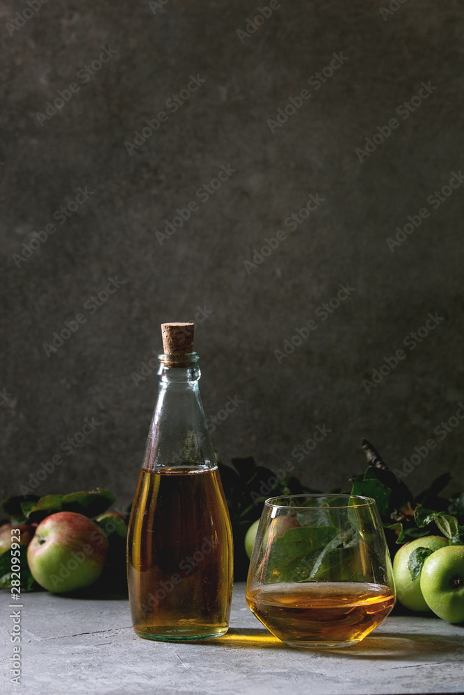 Bottle ang glass of apple juice with garden apples with leaves and branches on table with dark background. Autumn home harvesting. Bottle ang glass of apple juice with garden apples with leaves and branches on table with dark background. Autumn home harvesting.