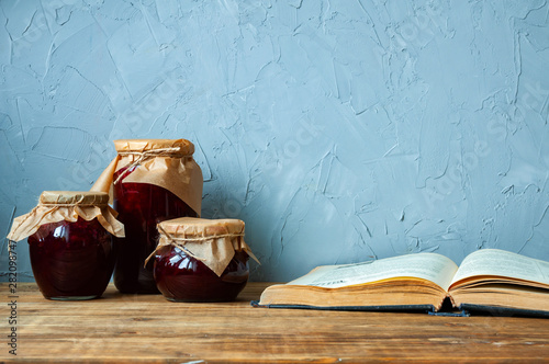 Three jars of jam and a recipe book on a wooden table photo