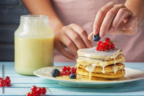 A girl in a pink apron decorates pancakes with blueberries and red currants. Tasty pancakes with condensed milk. Close-up photograph of fresh natural dessert.