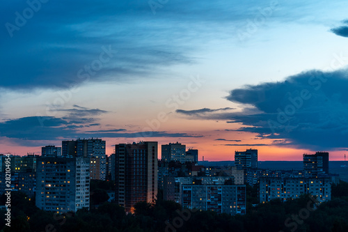 Before us the setting sun barely illuminates the high-rise buildings of one of the districts of Perm. Forest visible in the distance. Late evening, summer, July.