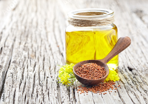 Fotografi Camelina oil with sedds and flowers on wooden background