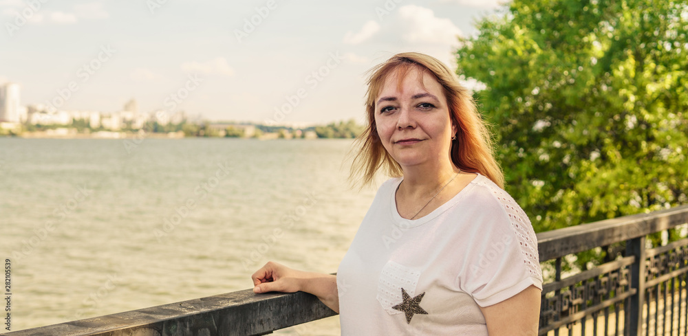 Portrait of a beautiful smiling woman is standing on the waterfront near the water.