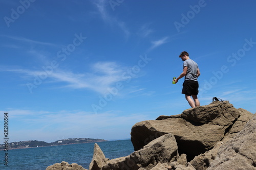 Person standing on rock by sea holding green water bottle 