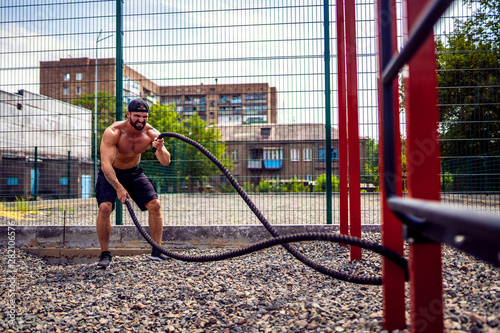 Athletic looking man working out with rope at street gym yard. Strength and motivation. Outdoor workout.