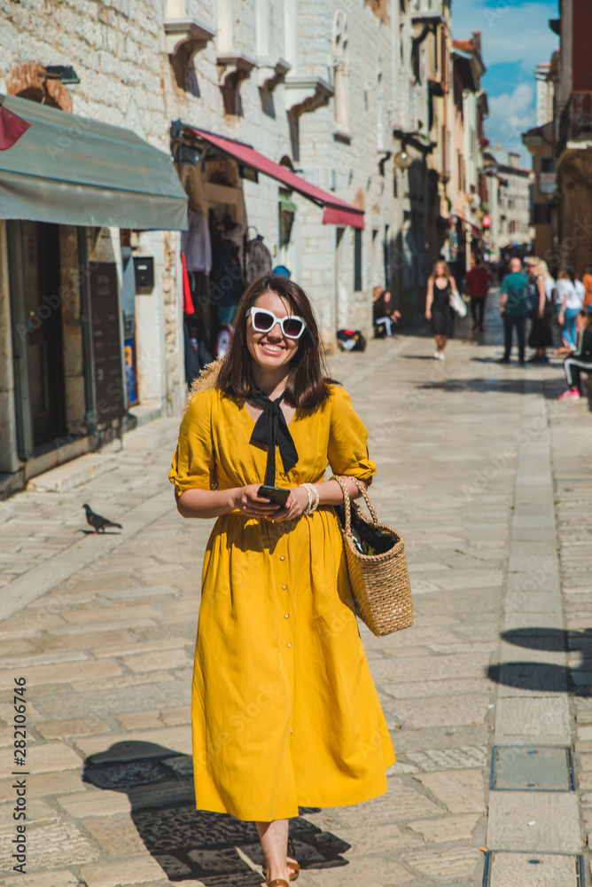 tourist woman in yellow sundress walking by small croatian city street