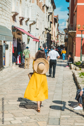 tourist woman in yellow sundress walking by small croatian city street © phpetrunina14