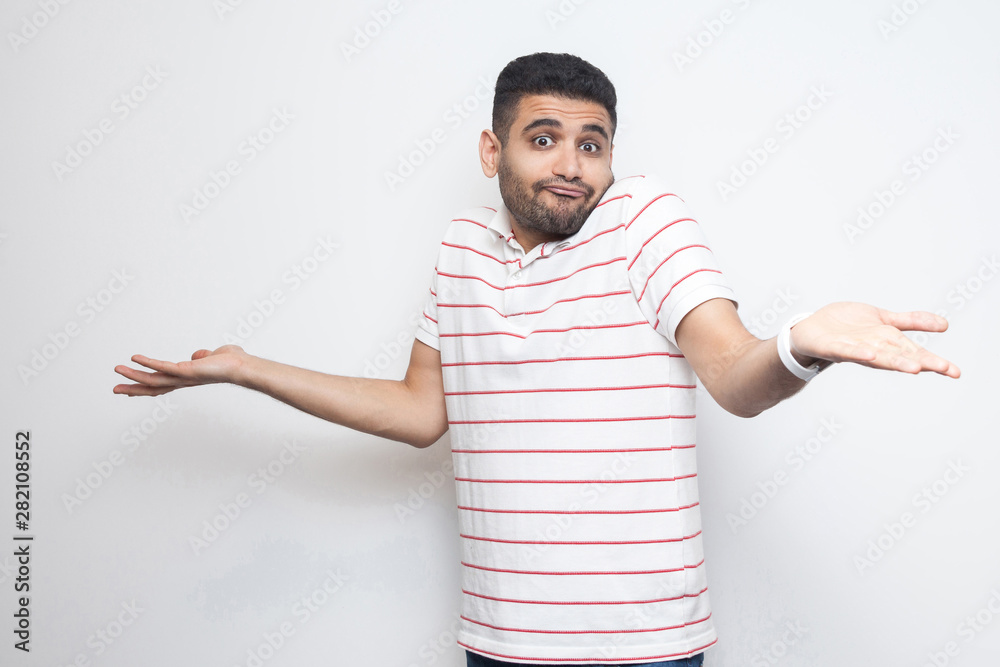 I don't know. Portrait of confused handsome bearded young man in striped t-shirt standing with raised arms and dont know what to do. indoor studio shot, isolated on white background. I don't know. Portrait of confused handsome bearded young man in striped t-shirt standing with raised arms and dont know what to do. indoor studio shot, isolated on white background.