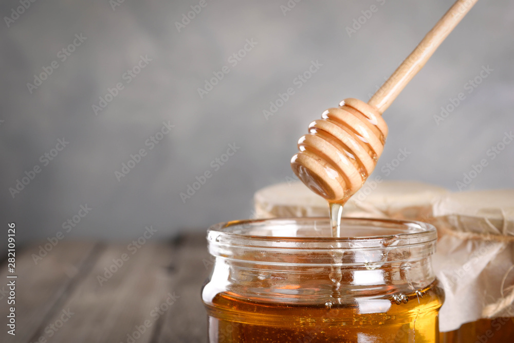 Pouring aromatic honey into jar, closeup. Honey in glass jars and honeycombs wax on wooden background. Wooden stick , instruments Pouring aromatic honey into jar, closeup. Honey in glass jars and honeycombs wax on wooden background. Wooden stick , instruments