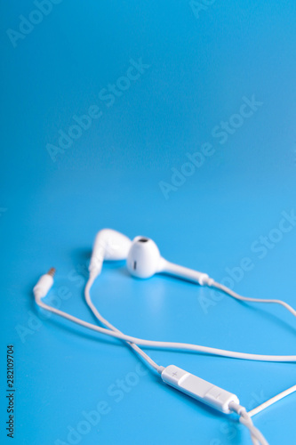 Mobile headphones of white color on a blue background in light colors with a place for text , copyspace. Top view.