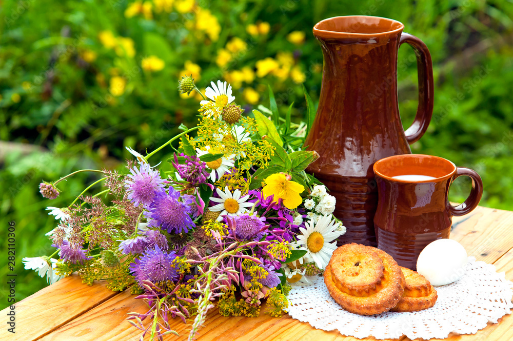 Still life with bouquet of wildflowers. Breakfast outdoors. Milk, buns, egg. Still life with bouquet of wildflowers. Breakfast outdoors. Milk, buns, egg.