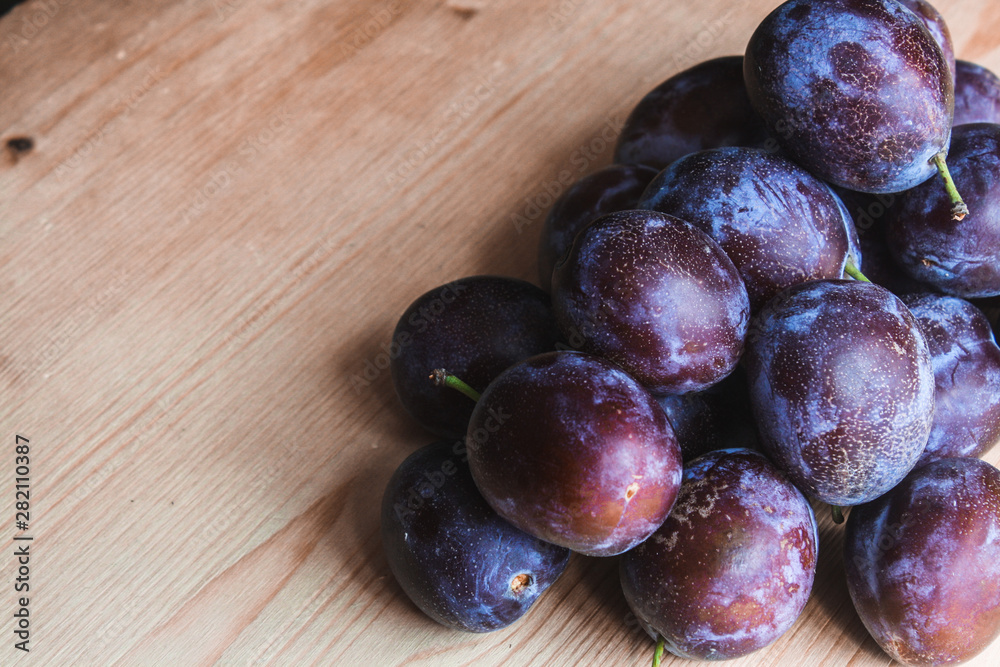 A pile of ripe plums on a wooden table, space