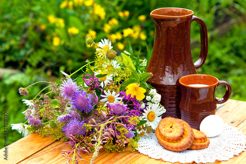 Still life with bouquet of wildflowers. Breakfast outdoors. Milk, buns, egg.	