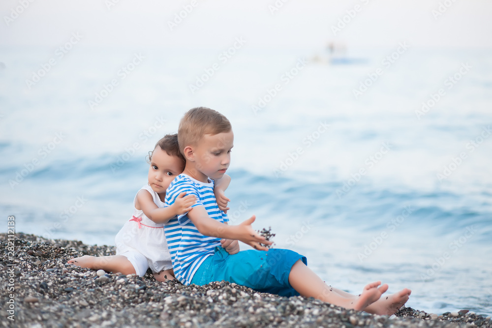 Boy in a striped t-shirt and little girl in white dress sitting close by the water at the beach Boy in a striped t-shirt and little girl in white dress sitting close by the water at the beach