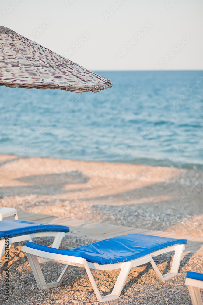 Obraz premium Sunbeds and umbrella on the beach by the sea. Beautiful concept for vacation, summer holidays and travel