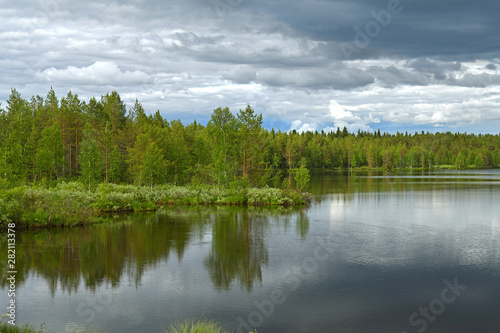 Northern forest lake with reflection of black clouds in water in Finnish Lapland. Kuusamo