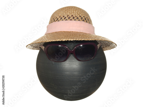 Lady's straw hat with pink ribbon and dark safety glasses on a black plastic ball isolated on a white background.