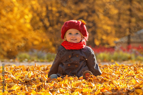 Happy autumn. A little girl in a red beret is playing with falling leaves and laughing.