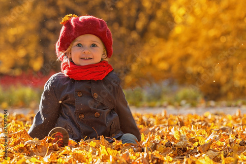 Happy autumn. A little girl in a red beret is playing with falling leaves and laughing.