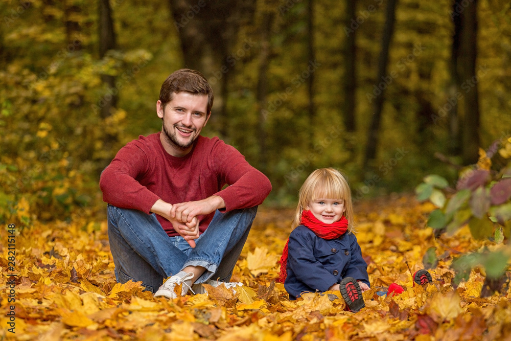Father and daughter are sitting and laughing in an autumn park.