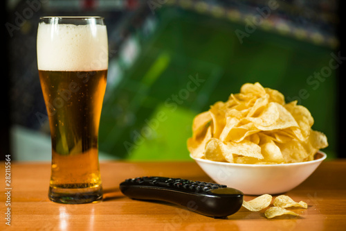 A glass of beer, a bowl of chips and a TV remote control on the TV screen photo