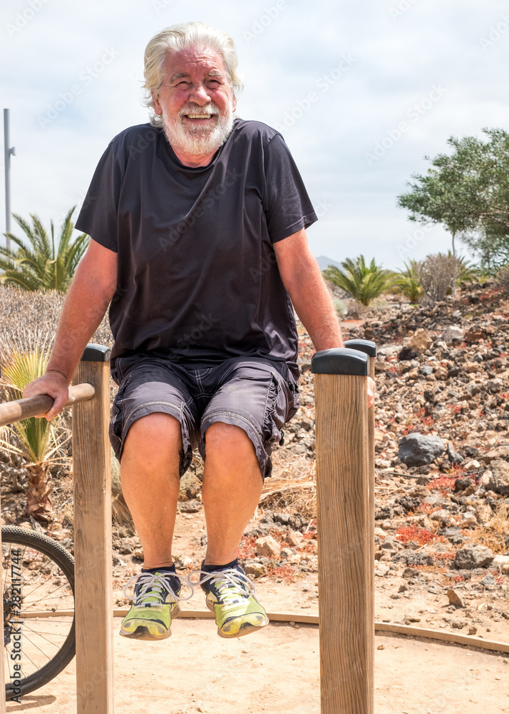Fototapeta premium Senior man in fitness activity outdoor in the park. 70 years and a healthy lifestyle. Bicycle close to him. Tropical place with palms