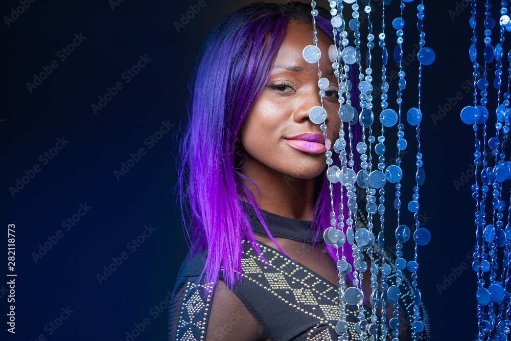 Dark-skinned model with purple hair. An African girl stands next to a  decorative curtain. Model