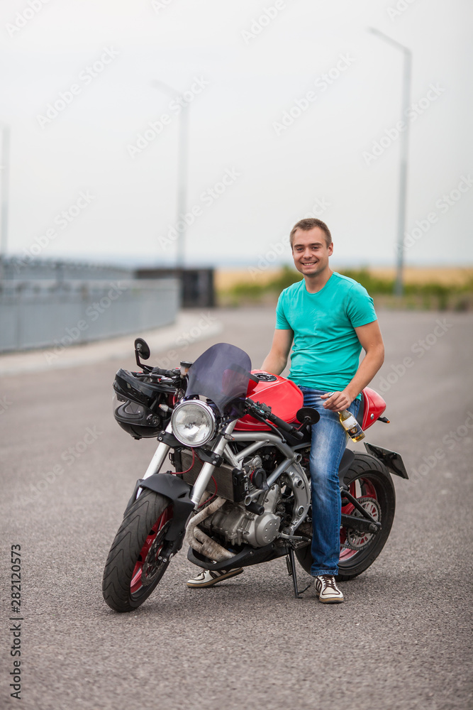 Handsome rider man sitting on classic style cafe racer motorbike on highway. Brutal fun urban lifestyle. young man holding bottle, sitting on motorcycle