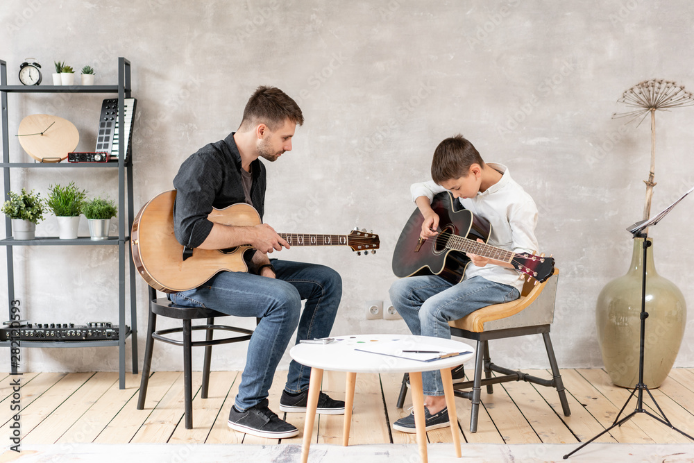 Two guys of different ages sit on chairs with guitars in their hands