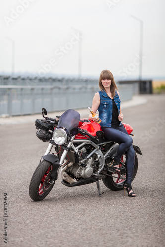 sexy biker woman sitting on a vintage custom motorcycle. Girl biker with perfect fit slim body. The spirit of freedom and independence. Beautiful brave woman is leaning on her motobike  on highway © Andrew