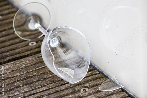 Zerbrochenes Weinglas liegt auf Holzdielen und zeigt die Spuren einer wilden Party mit Alkohol und alkoholisierten Gästen nach der Feier