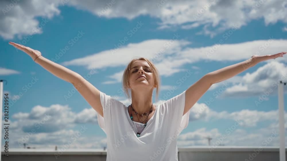 Close-up portrait of happy young woman putting hands in namaste mudra posture. Girl meditates in background of white clouds and blue sky. Camera shoots from below in slow motion Close-up portrait of happy young woman putting hands in namaste mudra posture. Girl meditates in background of white clouds and blue sky. Camera shoots from below in slow motion