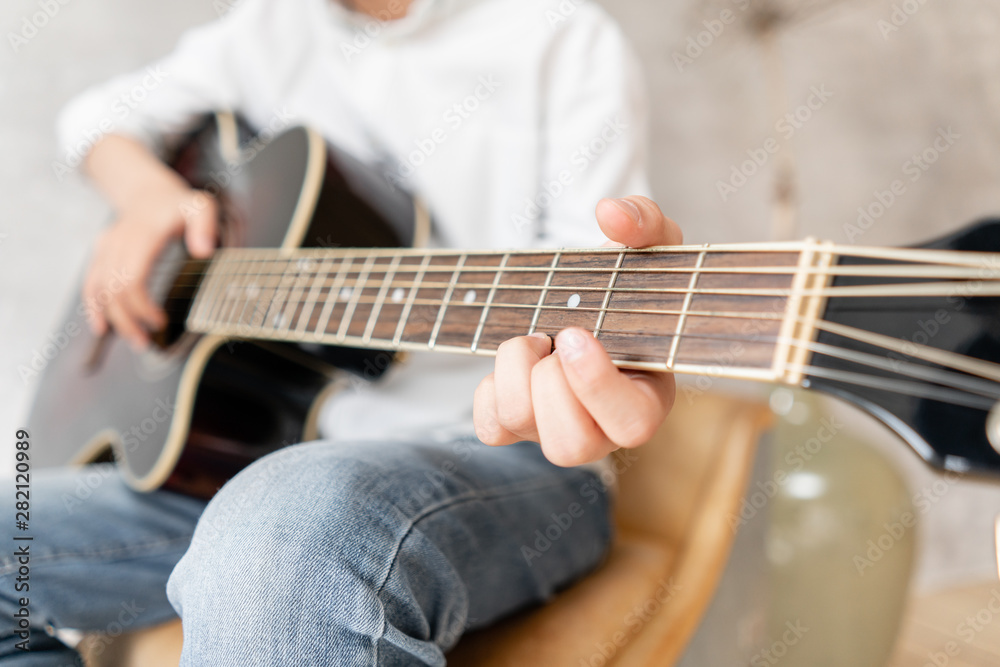 Closeup of wooden guitar in hands of young boy in casual clothes