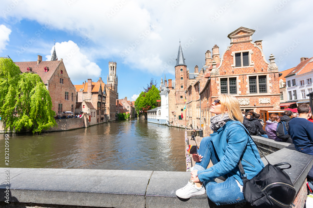 Fototapeta premium A young woman with the flag of Belgium in her hands is enjoying the view of the canals in the historical center of Bruges.