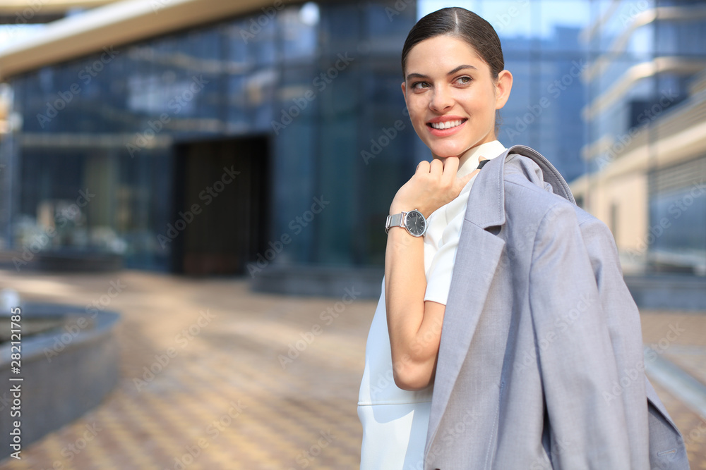 Smiling business woman standing with a jacket over her shoulder near office building. Smiling business woman standing with a jacket over her shoulder near office building.