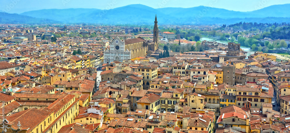 Aerial view. Top of buildings in the old city with Basilica di Santa Croce in a distance and green hills in the background. Panoramic skyline. Italy, Florence