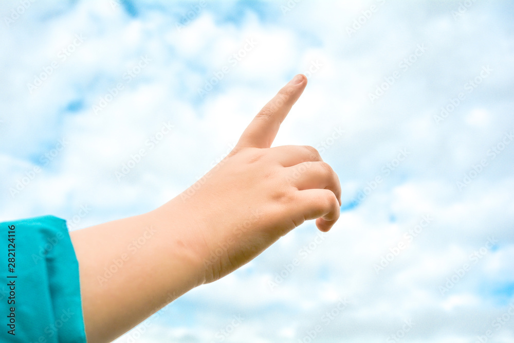Child hand with exposed index finger raised up over blue sky and clouds. Gesture