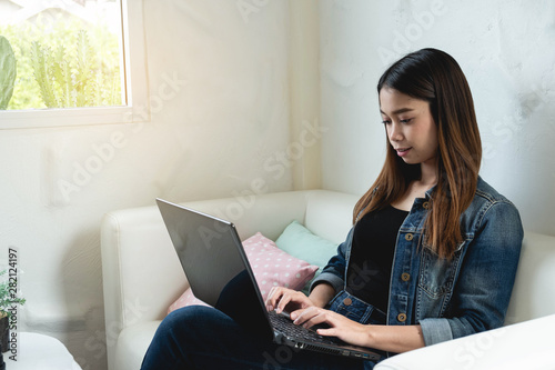 Asian woman sitting on sofa while useing computer laptop in the house, working business and ecucation concept photo