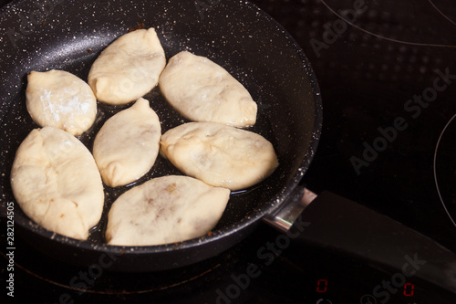 Meat pies, pan-fried in boiling oil. small raw pies in a frying pan with hot oil. copy space for text.
