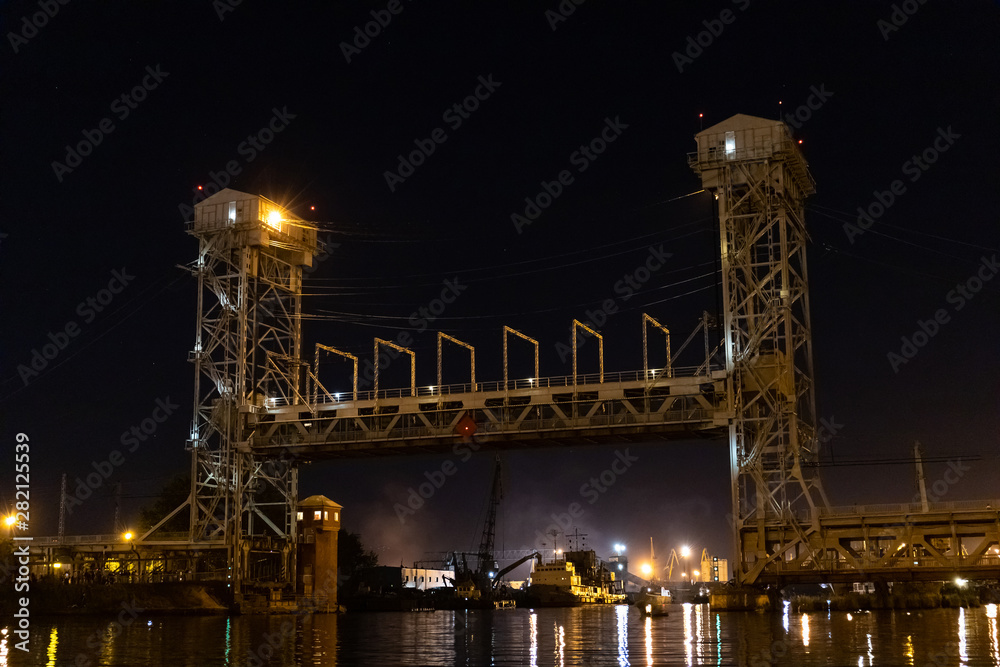 large iron bridge with two high towers over the river in the lights of lanterns at night