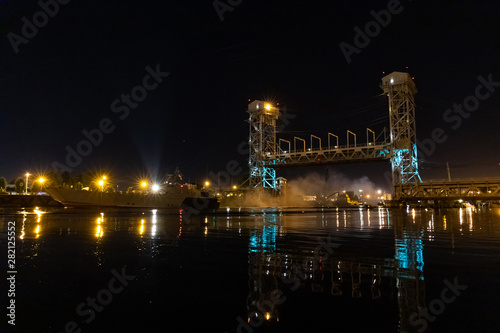 large iron bridge with two high towers over the river in the lights of lanterns at night